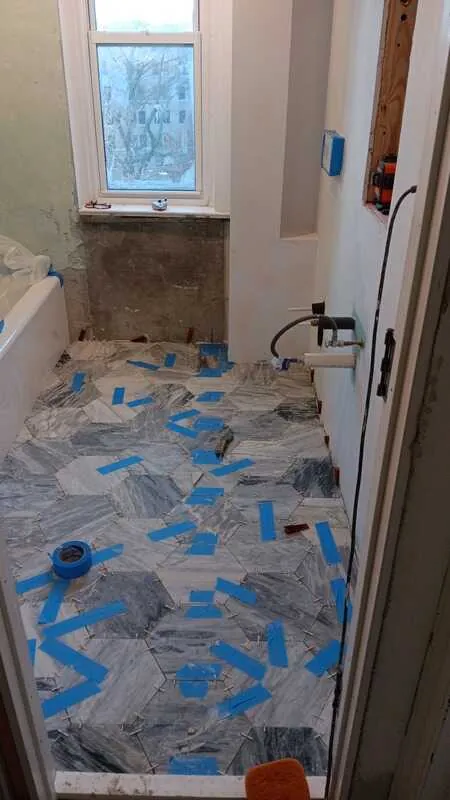 Grey and white marble hexagon tile laid on a bathroom floor, still taped off